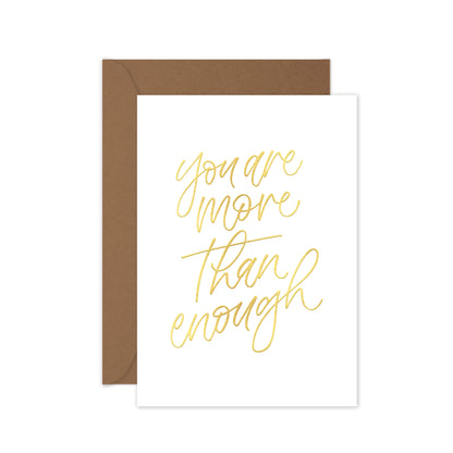 Greeting card with wrods 'You are more than enough' in gold foil, brown envelope on a white background