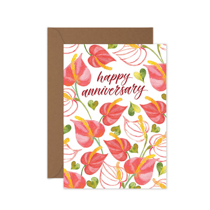 A greeting card with a floral pattern and the text 'Happy Anniversary' on the front, accompanied by a brown kraft envelope.