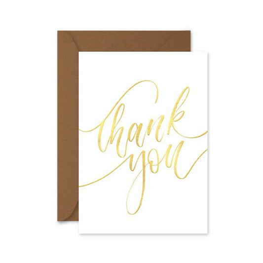 A folded white thank you card with gold foil lettering, accompanied by a brown kraft envelope, both displayed on a white background.